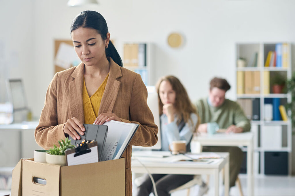 Upset businesswoman packing her things with coworkers in backdrop